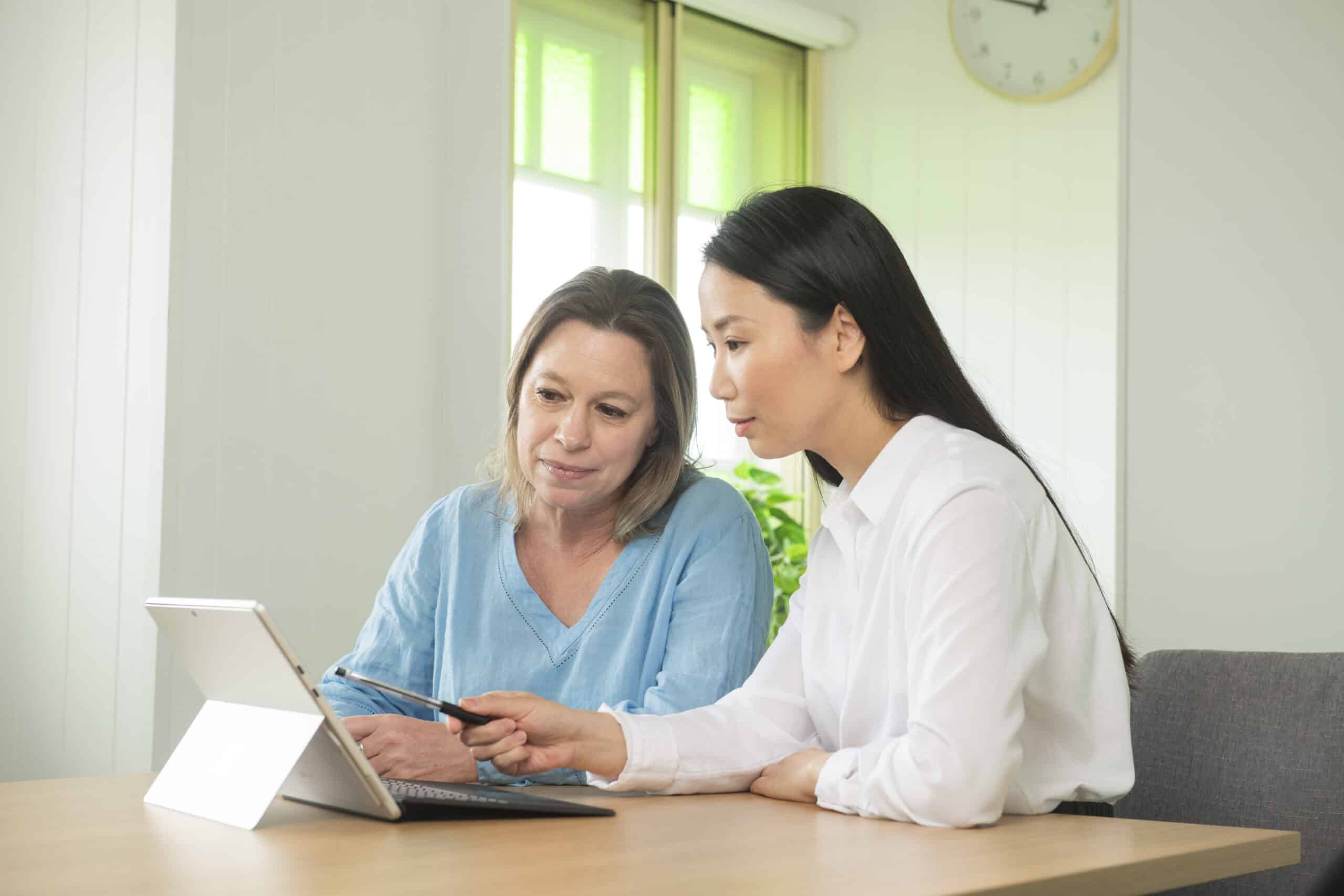Webinars Two women seated at a table, focused on a laptop screen, engaged in discussion.